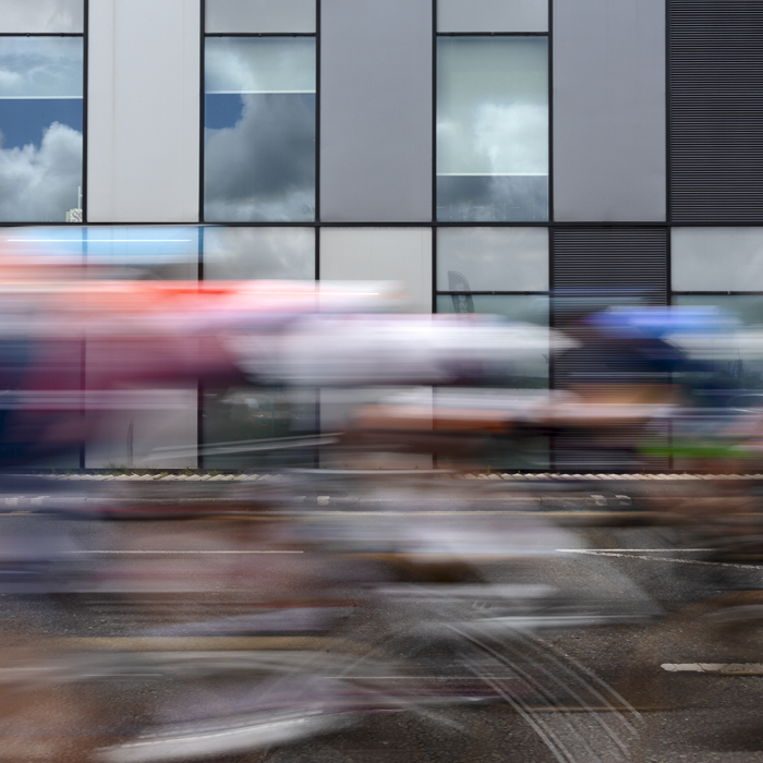 Tour of Britain Women’s 2024 - Riders speed past a modern office block in Warrington