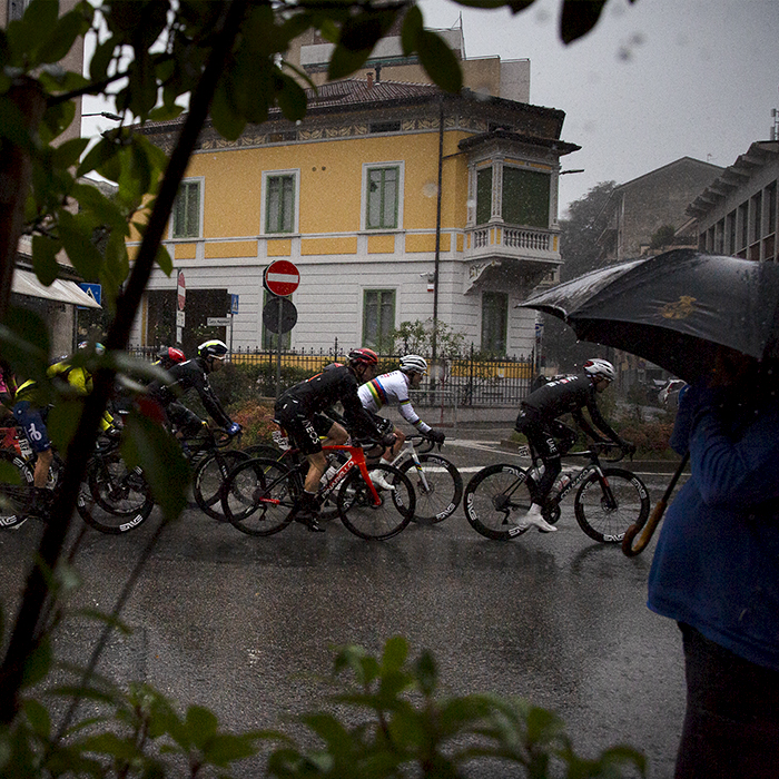 Tre Valli Varesine 2024 - Riders pass by a spectator huddled under an umbrella during the rain soaked race