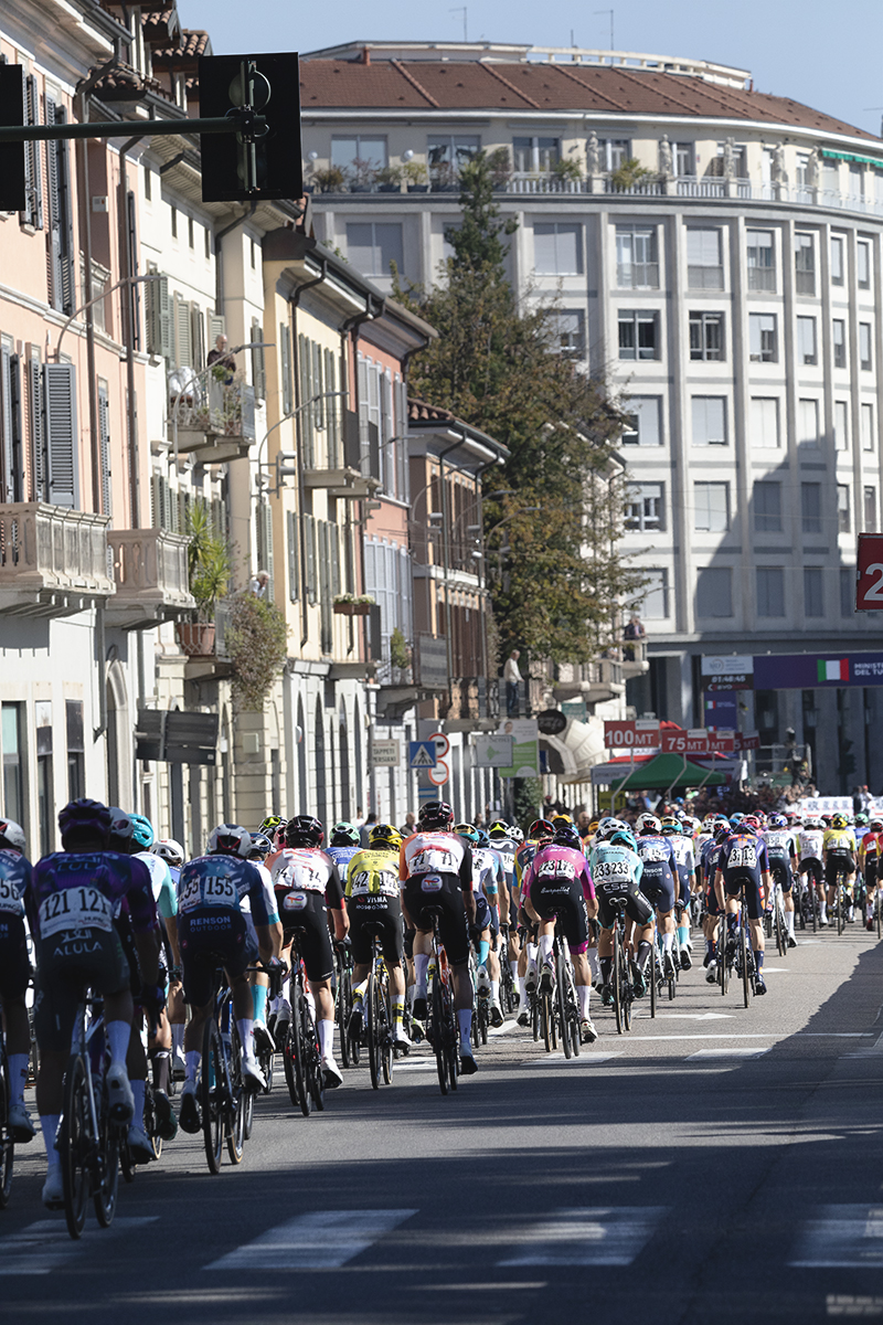 Tre Valli Varesine 2025 - The peloton from behind with buildings, both traditional and modern lining the streets in Varese
