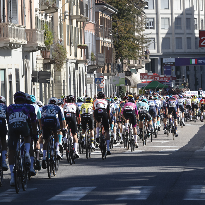 Tre Valli Varesine 2025 - The peloton from behind with buildings, both traditional and modern lining the streets in Varese