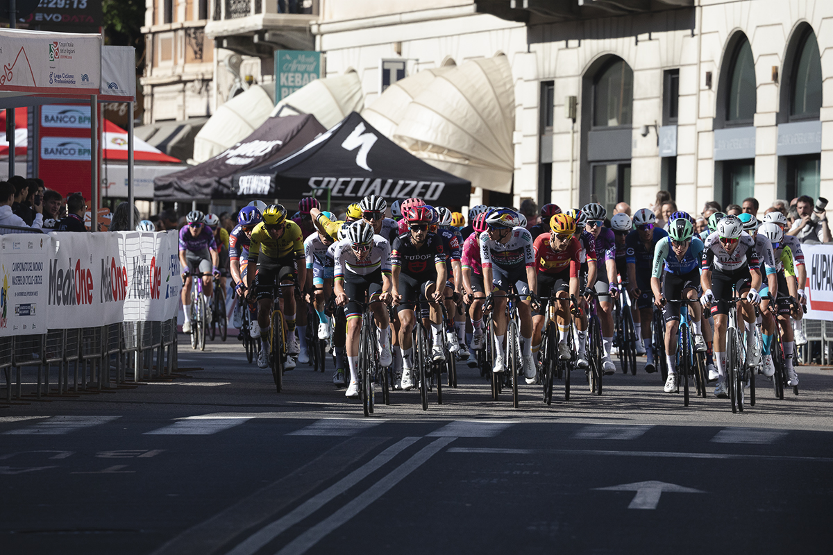 Tre Valli Varesine 2025 - Shop canopies can be seen in the background as the peloton rides through Varese
