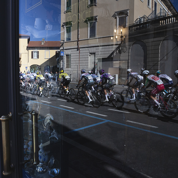 Tre Valli Varesine 2025 - The peloton is reflected in the window of an antiques shop