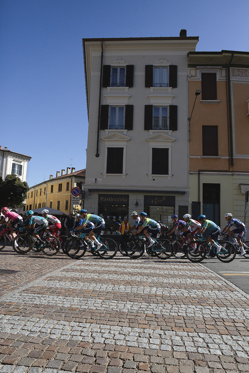 Tre Valli Varesine 2025 - Riders cross over a zebra crossing built into te brickwork of the road surface in front of Pasticceria Buosi