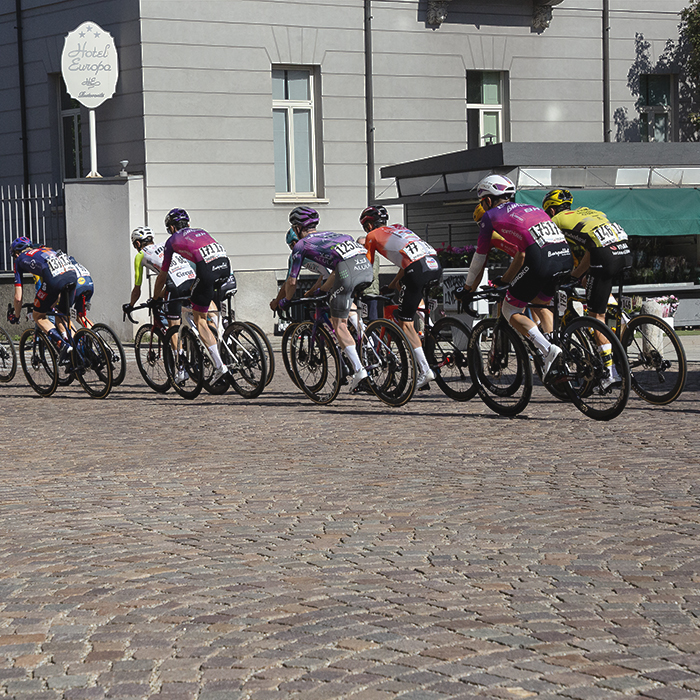 Tre Valli Varesine 2025 - The peloton seen riding over ornate cobbles in the centre of Varese