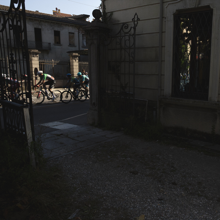Tre Valli Varesine 2025 - Riders seen through ornate iron gates in Varese