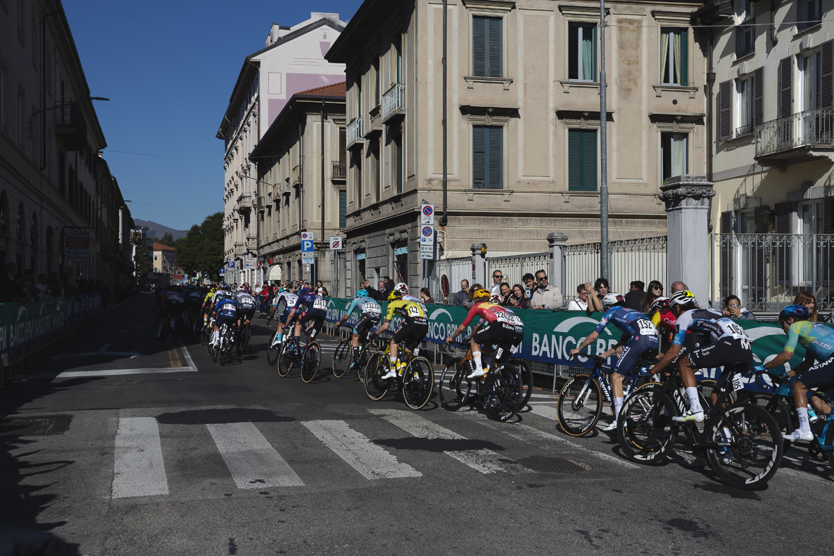 Tre Valli Varesine 2025 - Riders are watched by supporters as they ride past traditional rendered buildings