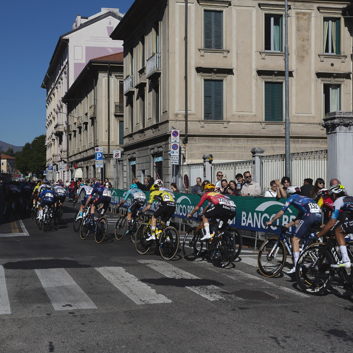 Tre Valli Varesine 2025 - Riders are watched by supporters as they ride past traditional rendered buildings