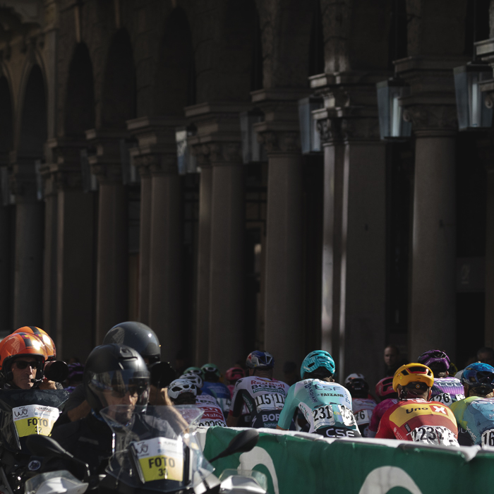 Tre Valli Varesine 2025 - The columns of an arcade are seen in the background as riders pass through the city as the moto photographers watch on