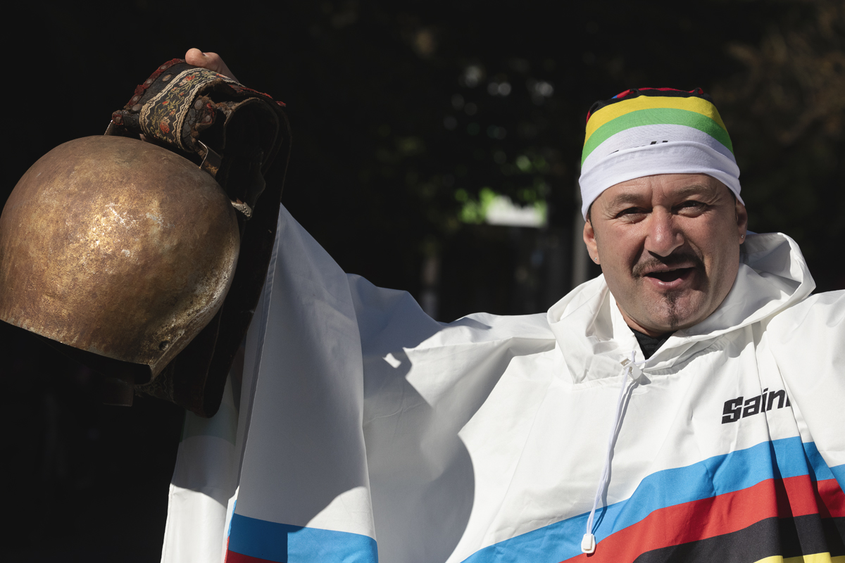 Tre Valli Varesine 2025 - A fan dressed in a UCI World Champion’s poncho holds aloft an enormous cow bell