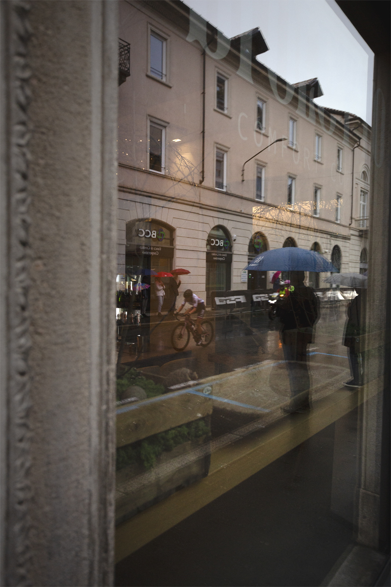 Tre Valli Varesine Women’s Race 2024 - Riders and spectators with umbrellas reflected in the windows in Varese