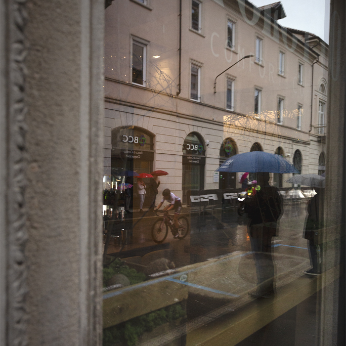 Tre Valli Varesine Women’s Race 2024 - Riders and spectators with umbrellas reflected in the windows in Varese