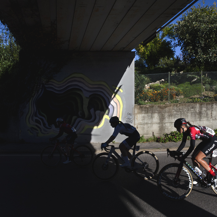 Tre Valli Varesine Women’s Race 2025 - Riders pass into the shadow of a modern road bridge which is decorated with an abstract mural