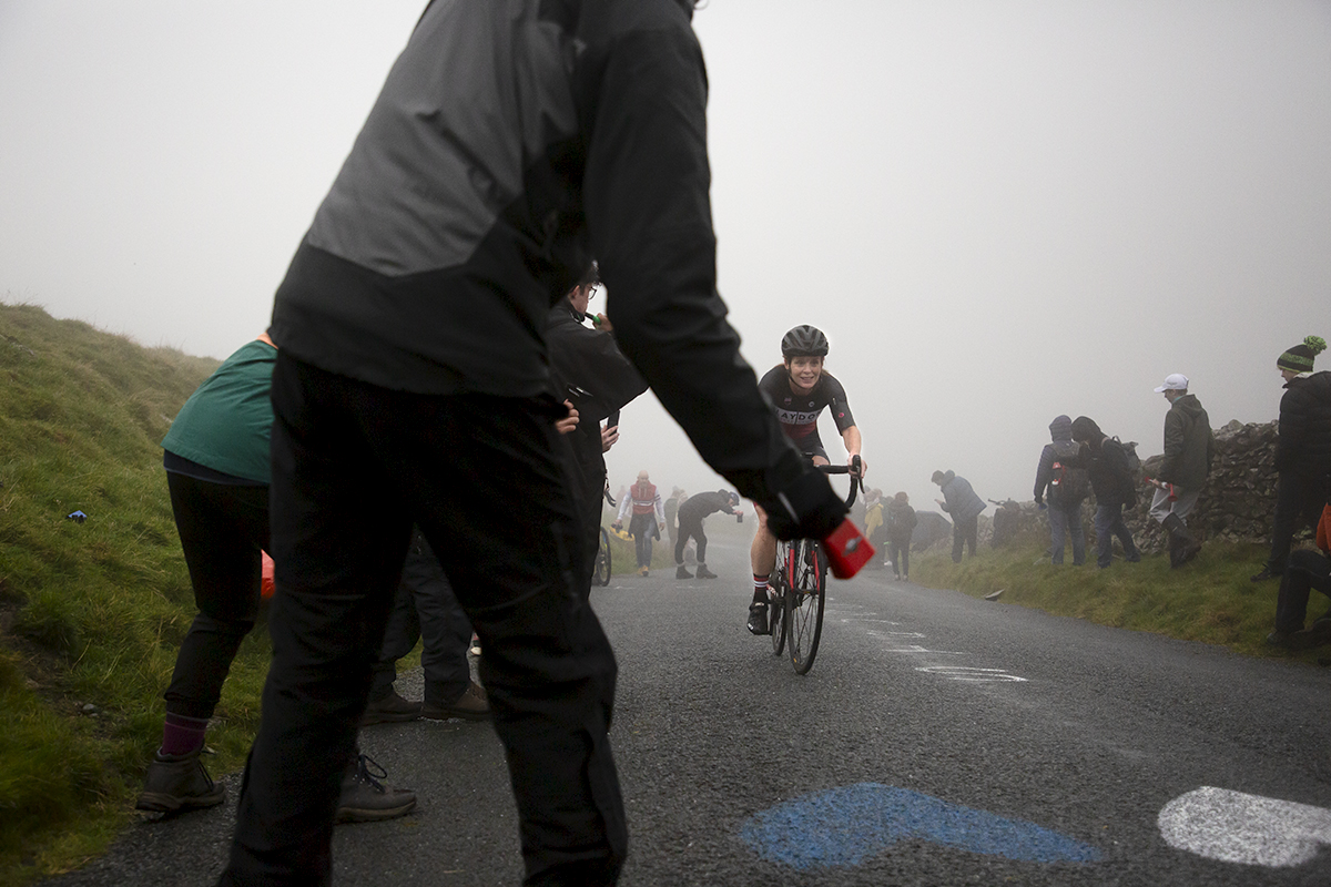 UK National Hill Climb Championships 2023 - A fan rings a cowbell at the side of the road as Anglea McGurk makes her way through murky conditions at the top of the climb