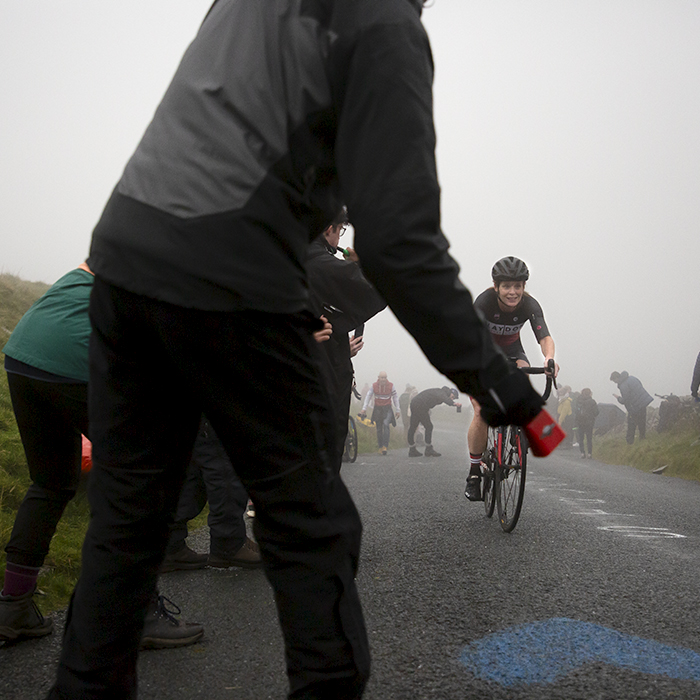 UK National Hill Climb Championships 2023 - A fan rings a cowbell at the side of the road as Anglea McGurk makes her way through murky conditions at the top of the climb