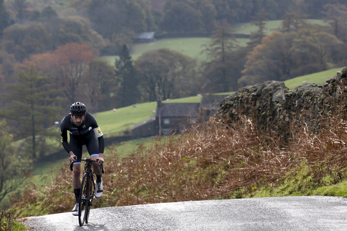 UK National Hill Climb Championships 2023 - Jude Taylor stands on his pedals and pushes up the climb with a Cumbrian farmhouse in the background