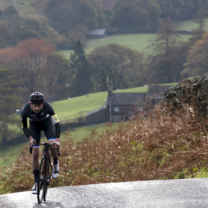 UK National Hill Climb Championships 2023 - Jude Taylor stands on his pedals and pushes up the climb with a Cumbrian farmhouse in the background