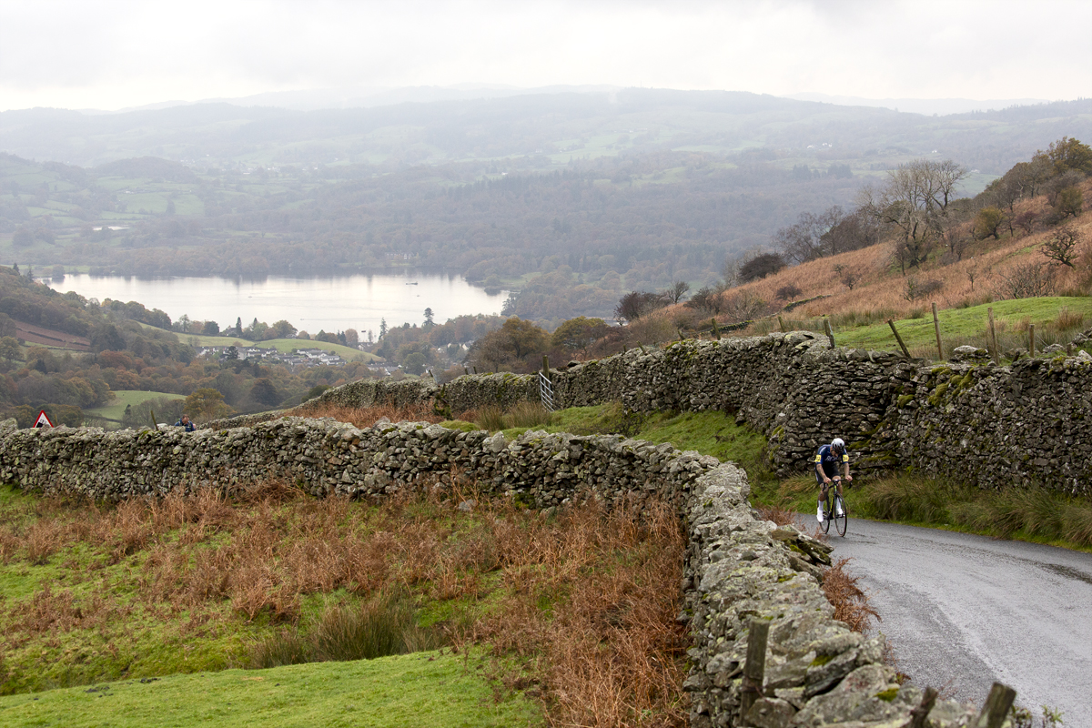 UK National Hill Climb Championships 2023 - Sam Fox is framed by dry stone walls with Lake Windermere in the background as he climbs the hill