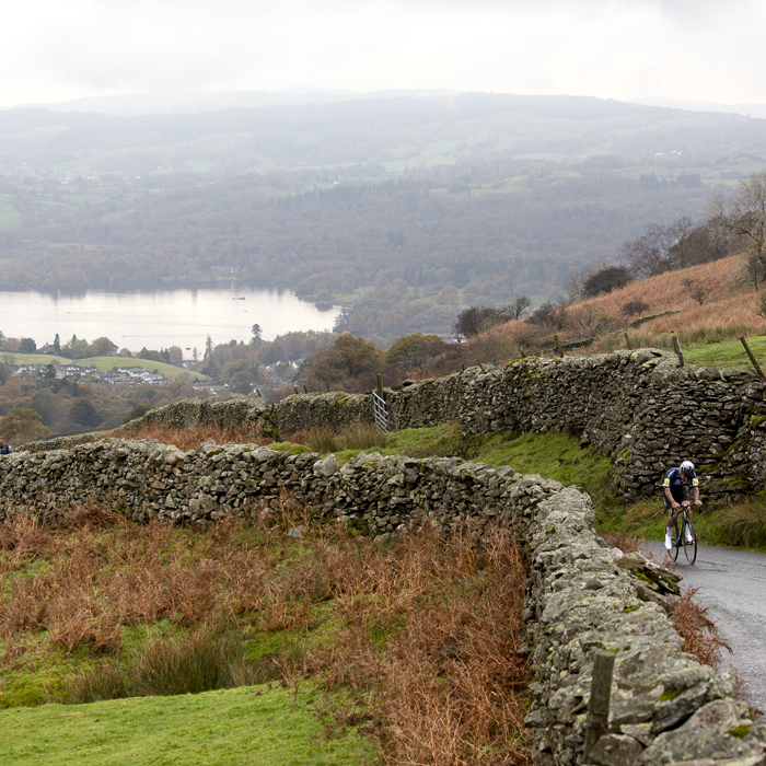 UK National Hill Climb Championships 2023 - Sam Fox is framed by dry stone walls with Lake Windermere in the background as he climbs the hill