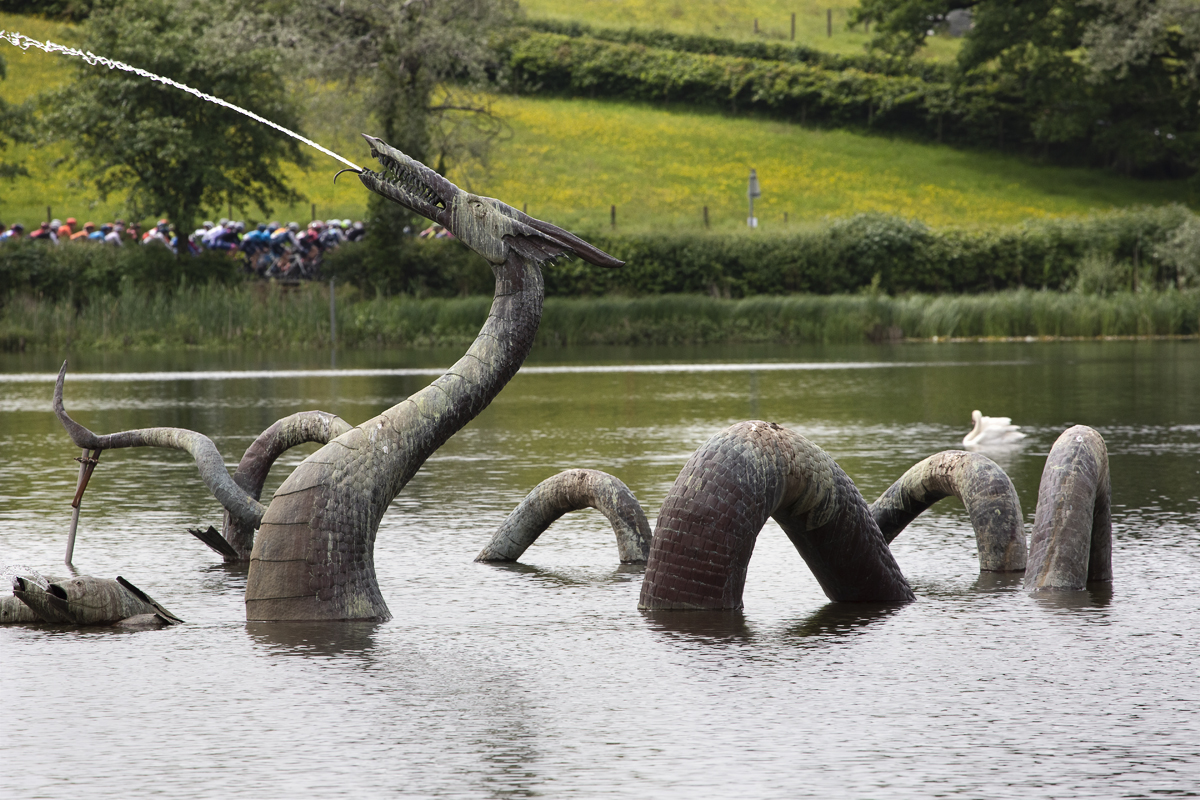 Women’s Tour 2019 - The women’s peloton are seen in the distance as a fountain shaped as a dragon spouts in the foreground in Llandrindod Wells