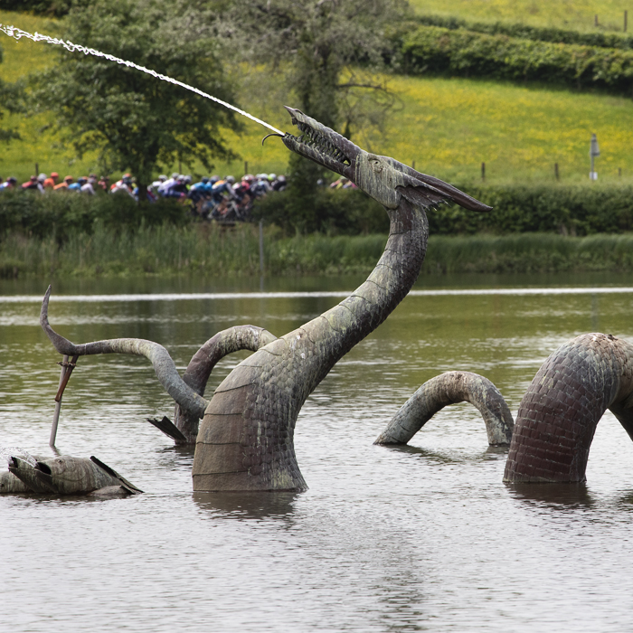 Women’s Tour 2019 - The women’s peloton are seen in the distance as a fountain shaped as a dragon spouts in the foreground in Llandrindod Wells