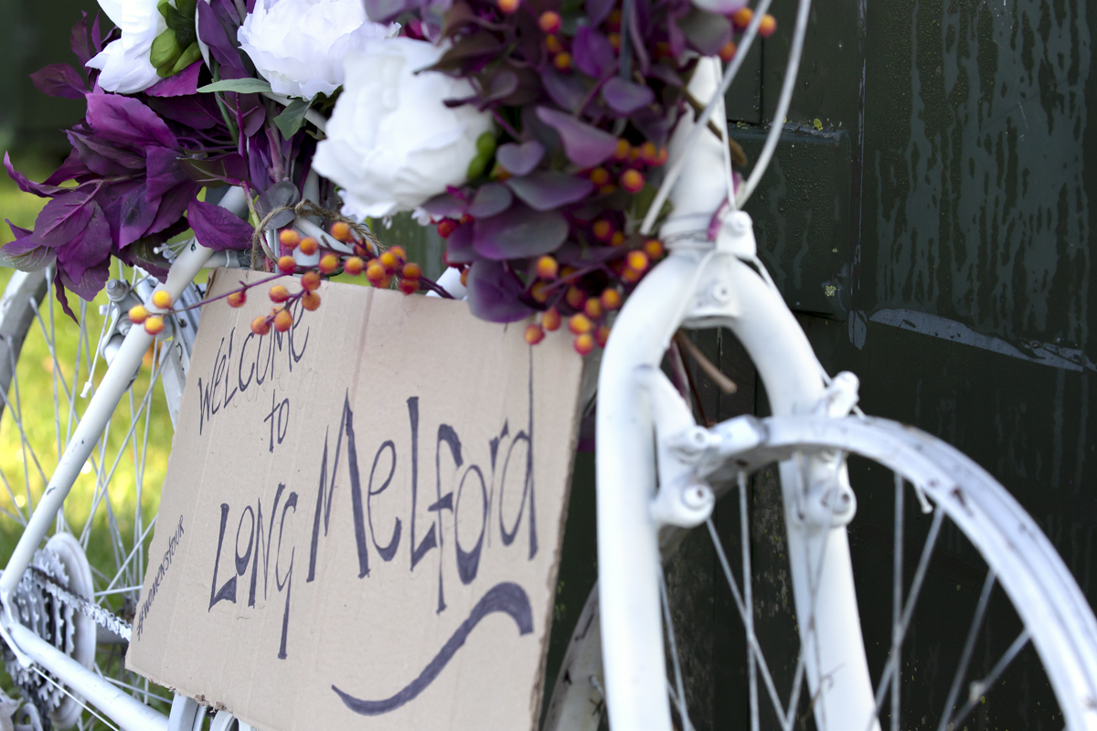 Women’s Tour 2021 - A bike at the side of the road is decorated with flowers and a sign reading welcome to Long Melford