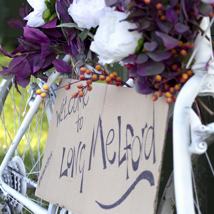 Women’s Tour 2021 - A bike at the side of the road is decorated with flowers and a sign reading welcome to Long Melford