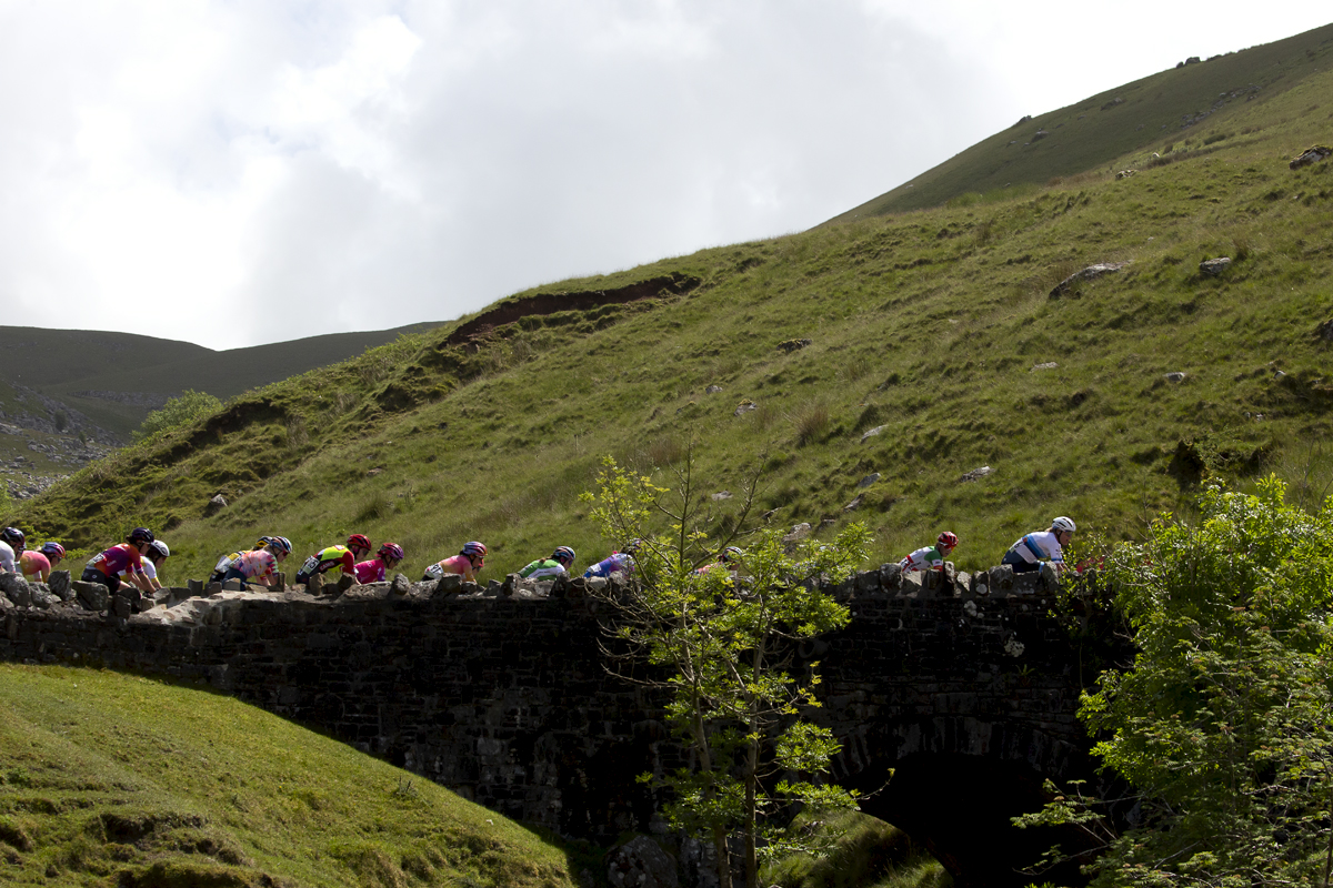 Women’s Tour 2022 - Riders cross a stone bridge over a brook on their way up the Black Mountain