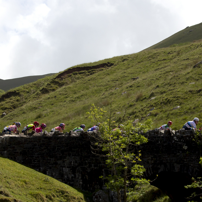 Women’s Tour 2022 - Riders cross a stone bridge over a brook on their way up the Black Mountain