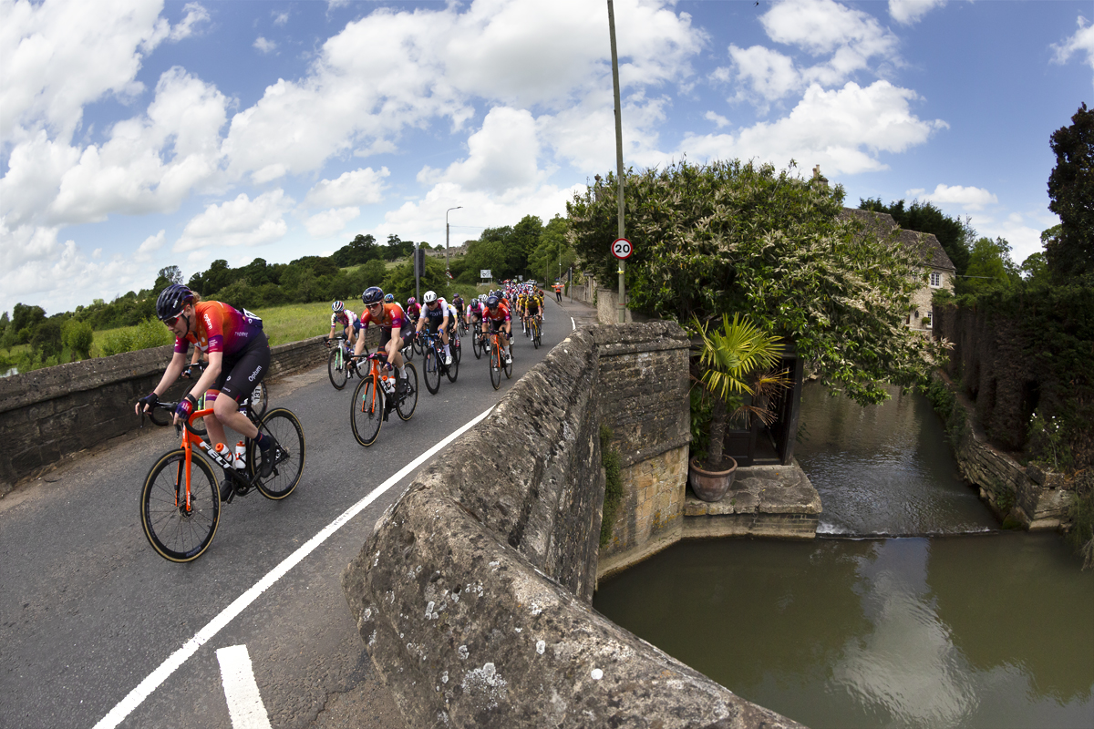 Women’s Tour 2022 - Riders cross a stone bridge on their way into the village