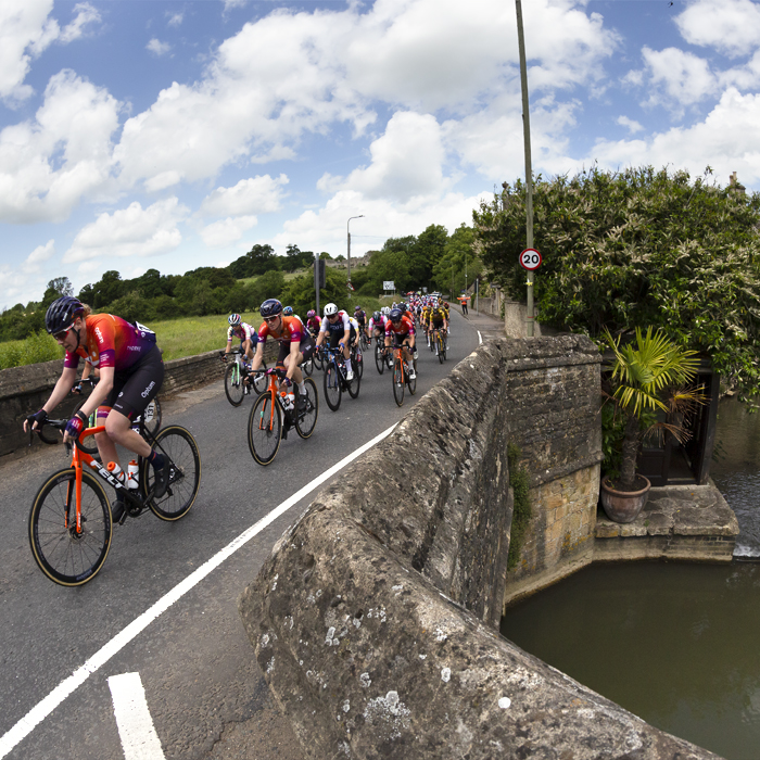 Women’s Tour 2022 - Riders cross a stone bridge on their way into the village