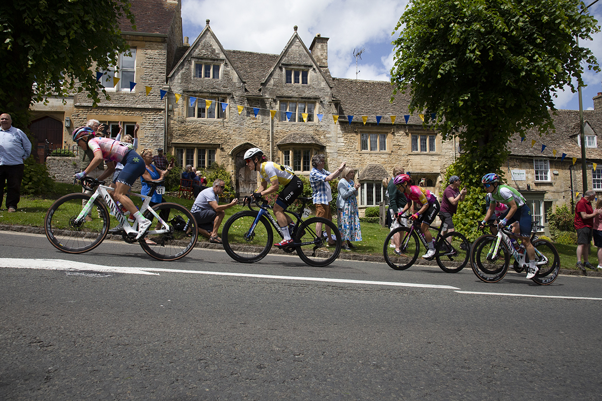 Women’s Tour 2022 - Riders make their way up the hill climb past spectators with Cotswolds stone cottages in the background