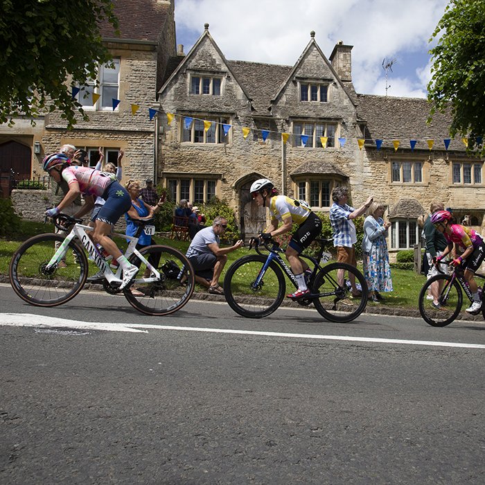 Women’s Tour 2022 - Riders make their way up the hill climb past spectators with Cotswolds stone cottages in the background